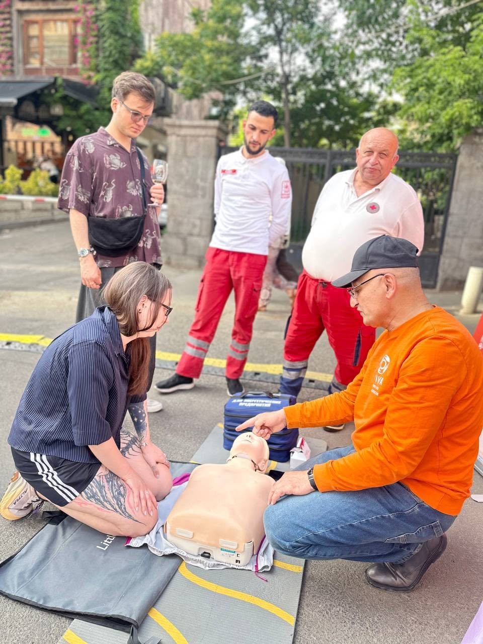 VIVA Foundation instructor in an orange shirt guiding a participant through CPR at a community event in Armenia