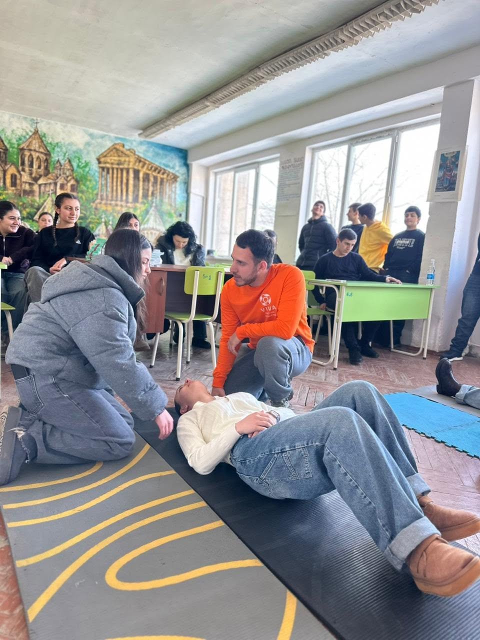 VIVA Foundation volunteer in an orange shirt coaching students during practical first aid training in Armenia