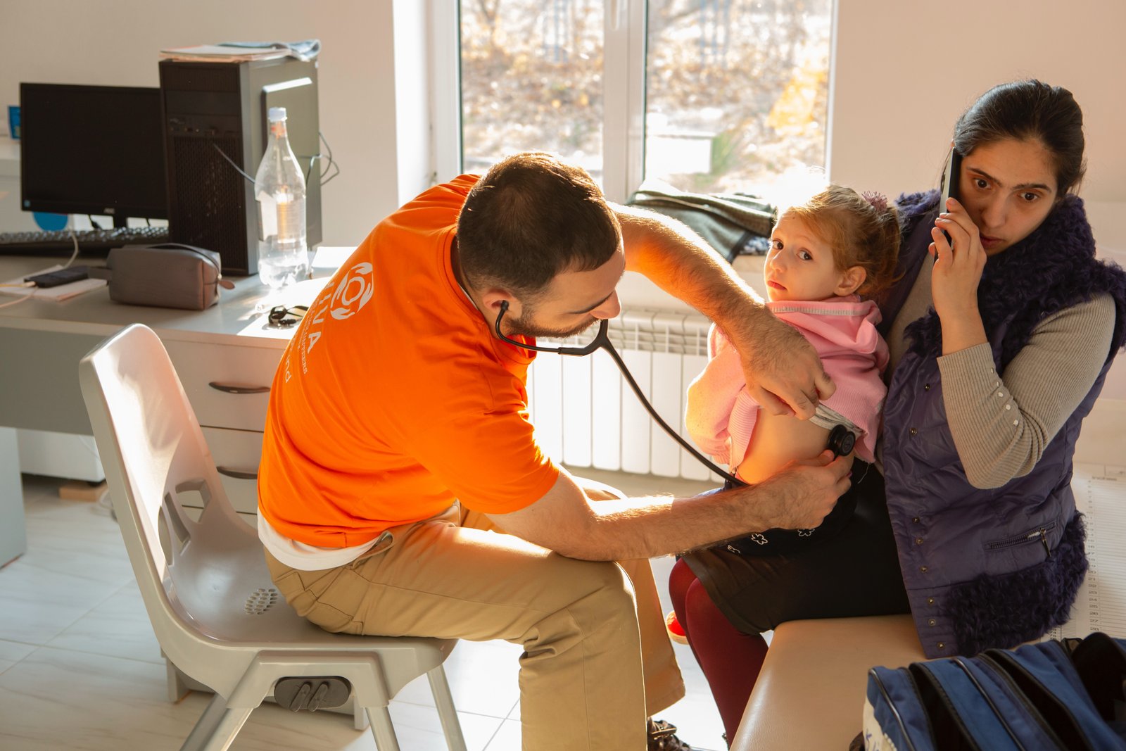 VIVA Foundation doctor in an orange volunteer shirt examining a child during a free medical consultation in Armenia