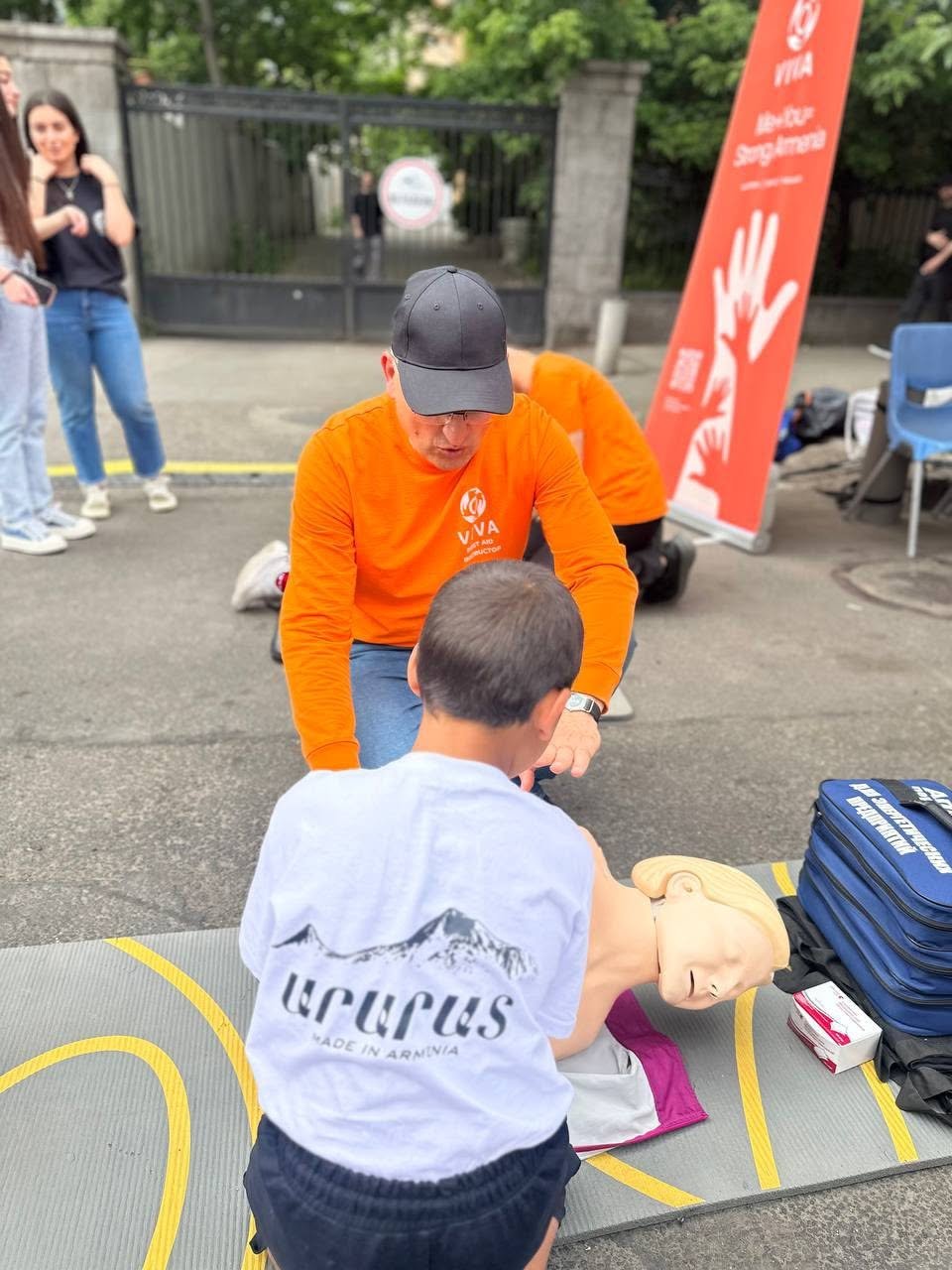 VIVA Foundation volunteer in an orange shirt teaching a young participant first aid at a public event in Armenia