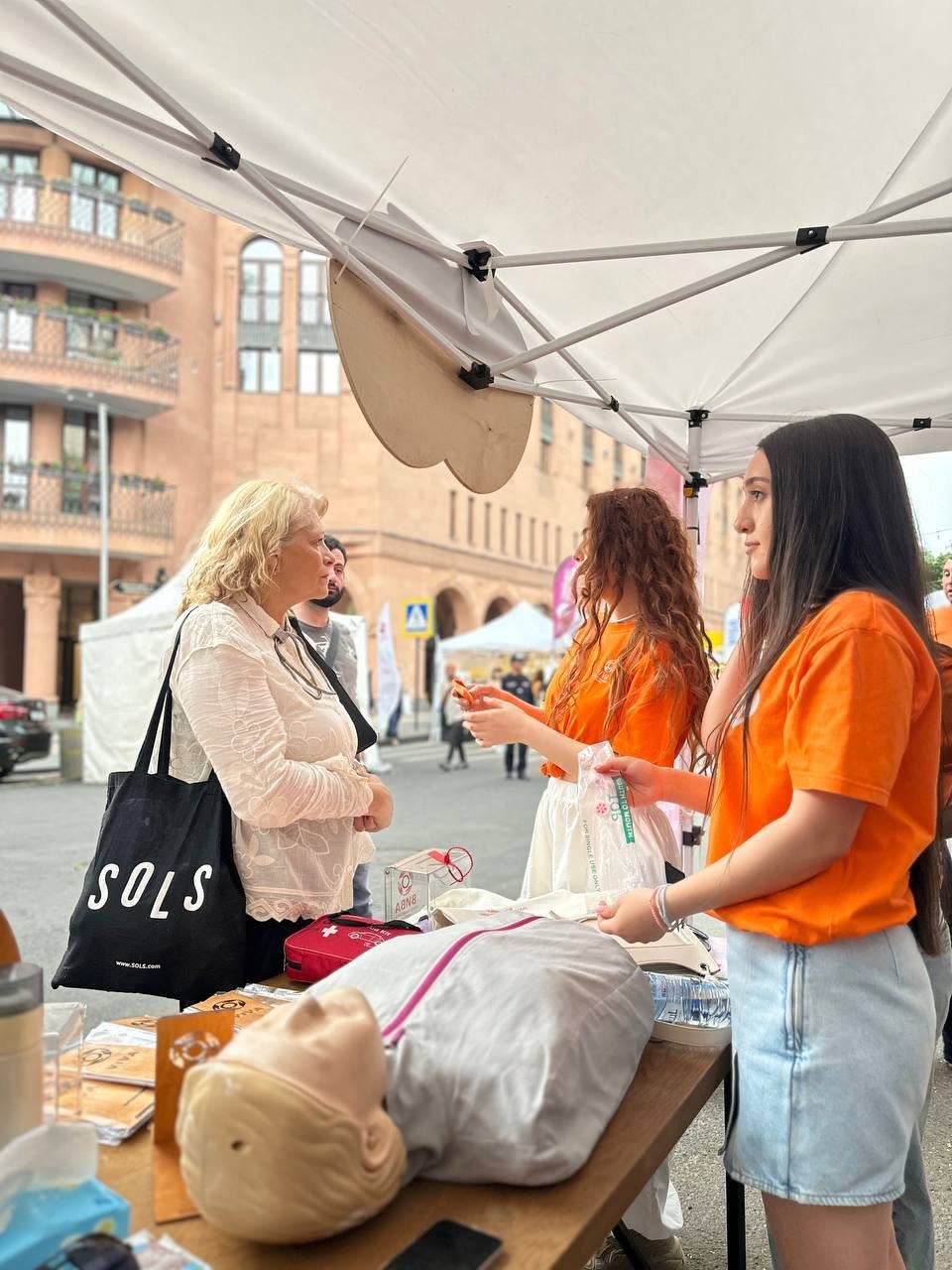VIVA Foundation volunteers in orange shirts speaking with visitors at a first aid outreach stand in Armenia
